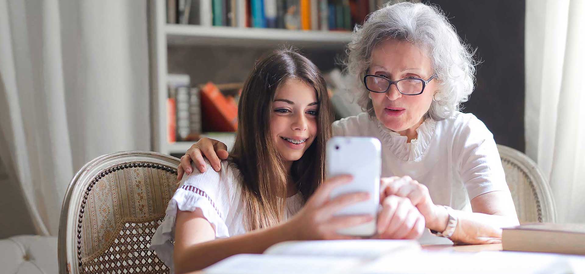 An elderly lady and a younger girl looking at something on the girl's phone